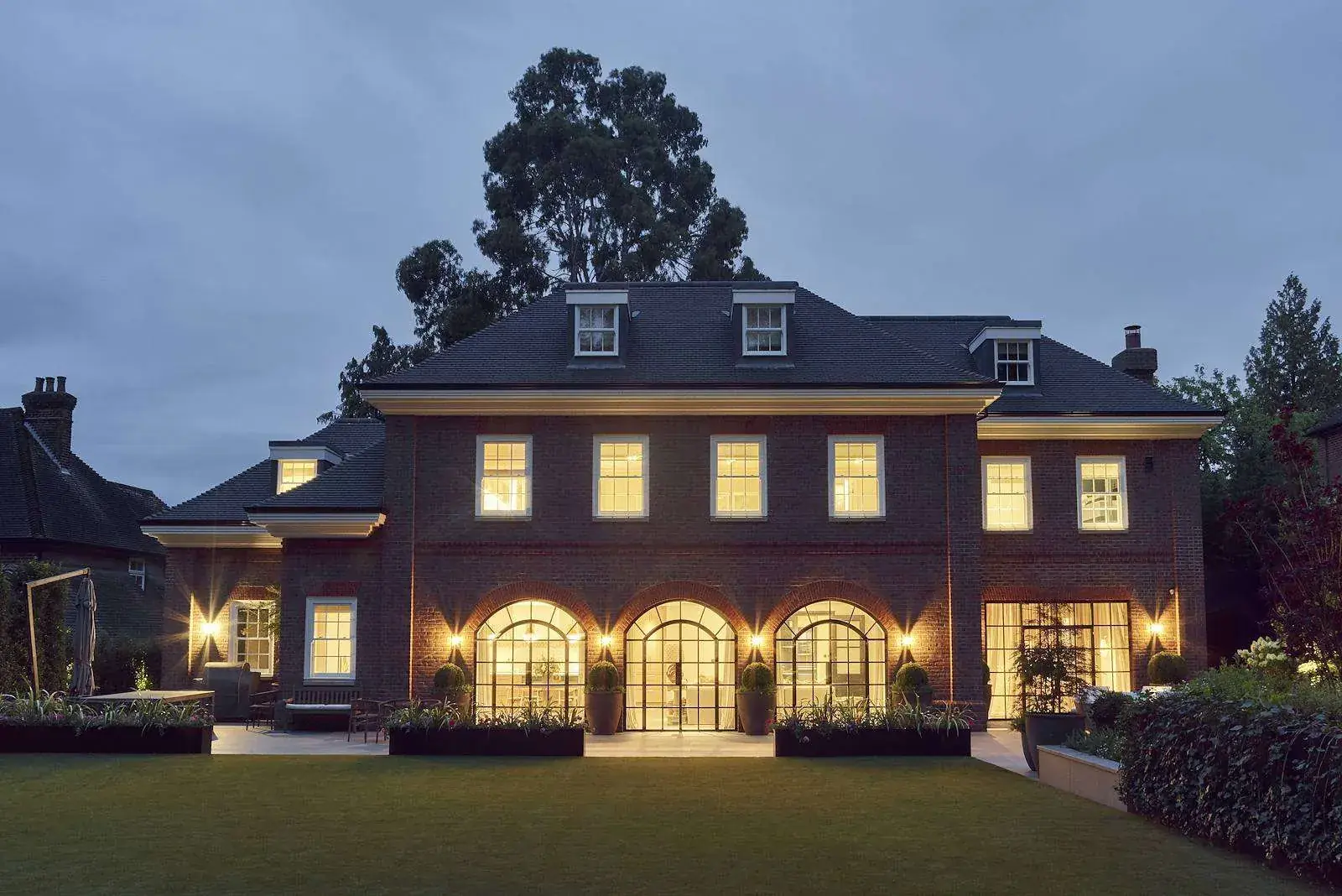 Large brick house at dusk with warm facade and window lighting