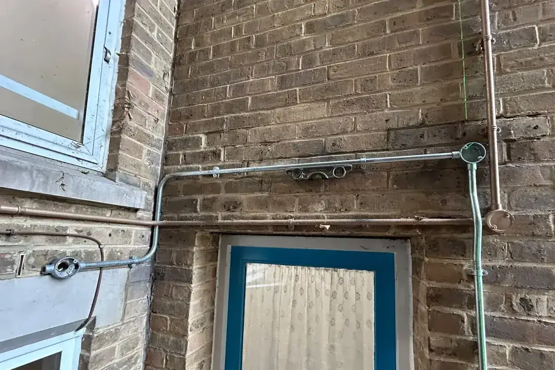 Galvanised steel conduit on the brick wall over an entrance at a sheltered housing scheme in Walthamstow