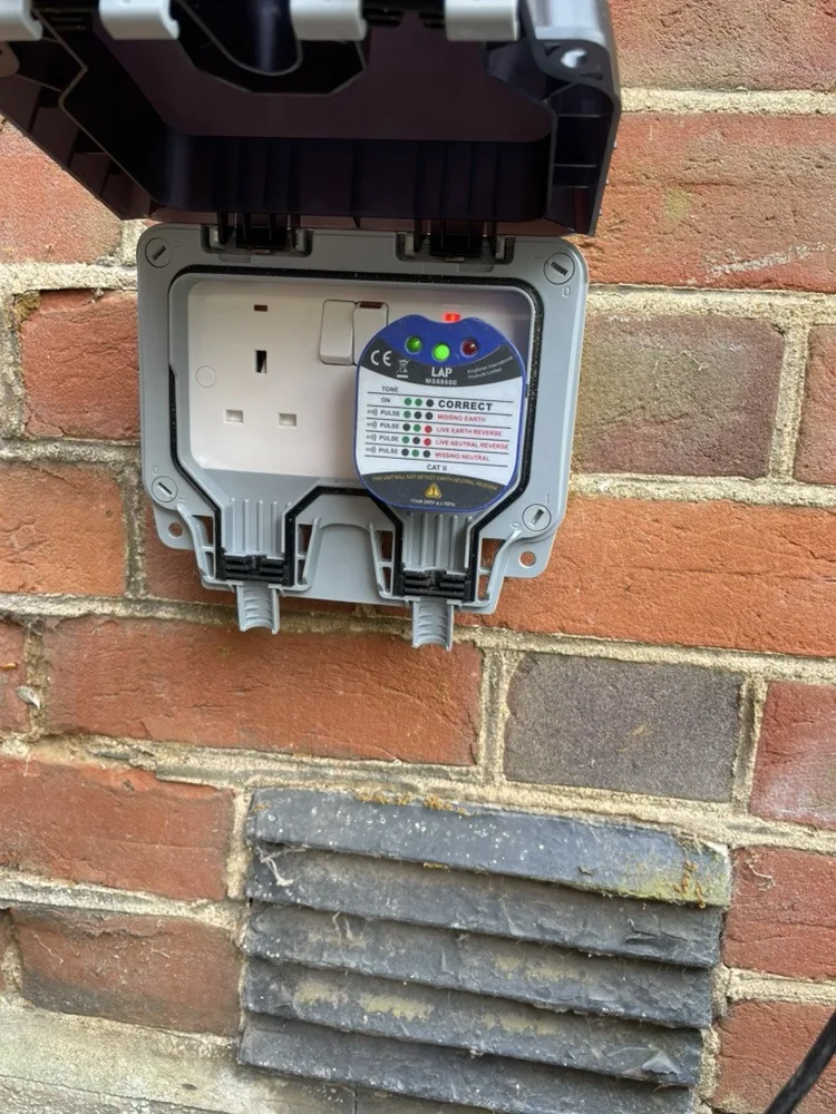 New weatherproof outdoor socket with a plug-in socket tester showing correct wiring