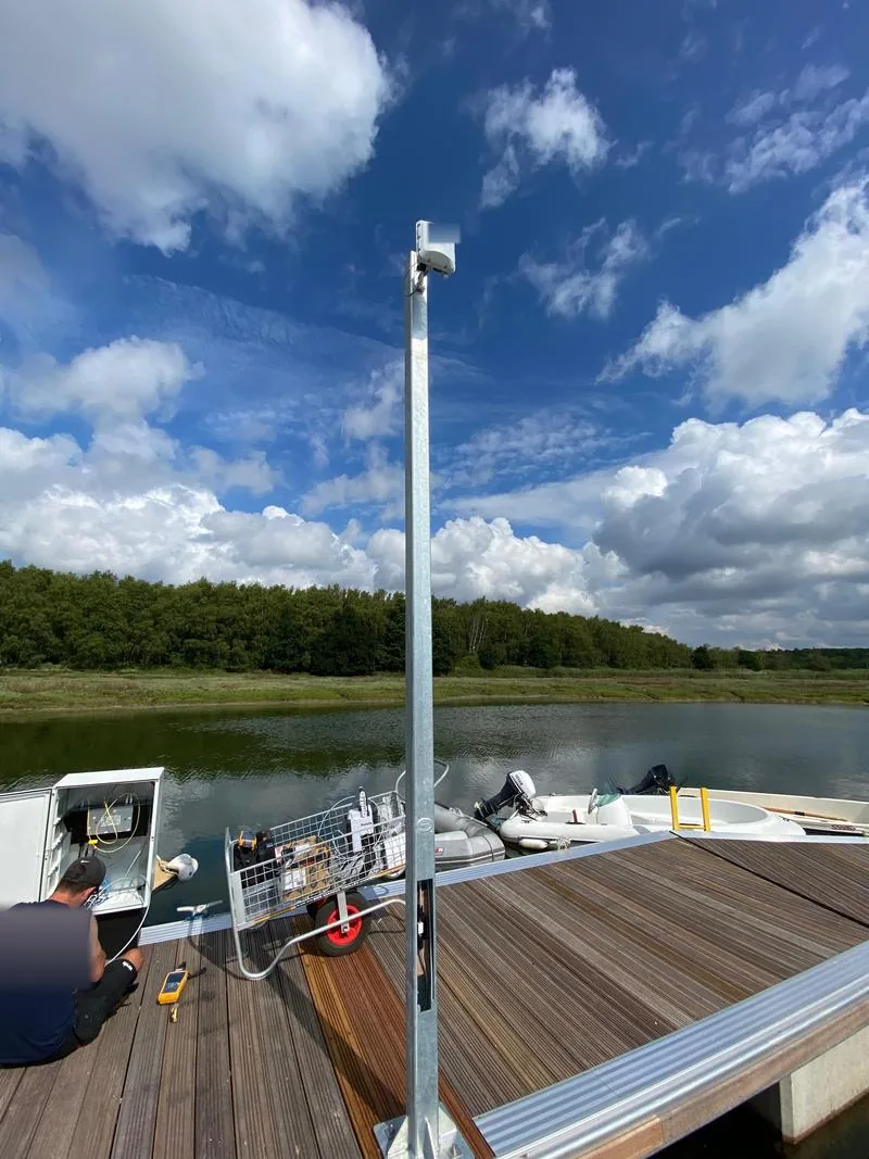 Engineer at a cabinet beside a pole-mounted outdoor access point on a marina